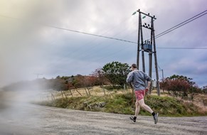 mann som jogger på grusvei forbi strømmast